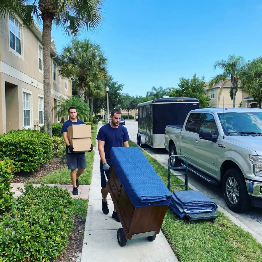Two movers walking furniture down a Florida sidewalk to the truck